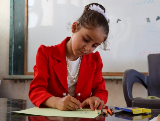 Sahar concentrates as she sits at a classroom desk drawing a picture.